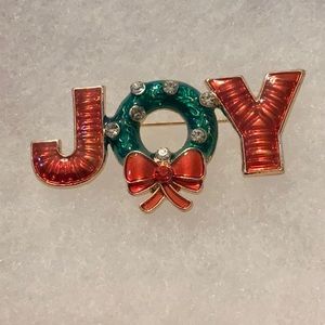 An enamel Christmas pin done in red and green spelling joy!